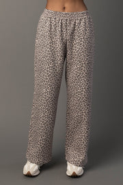 A person wearing Panache Apparel Collection’s Cream & Brown Leopard Sweatpants and white sneakers stands against a plain gray background. The photo shows the sweatpants from waist to feet.