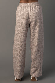A person wearing Panache Apparel Collection’s Blush & Light Brown Leopard Sweatpants, featuring a loose fit and high-waisted design with a blush and light brown leopard print, stands facing away against a plain grey background.