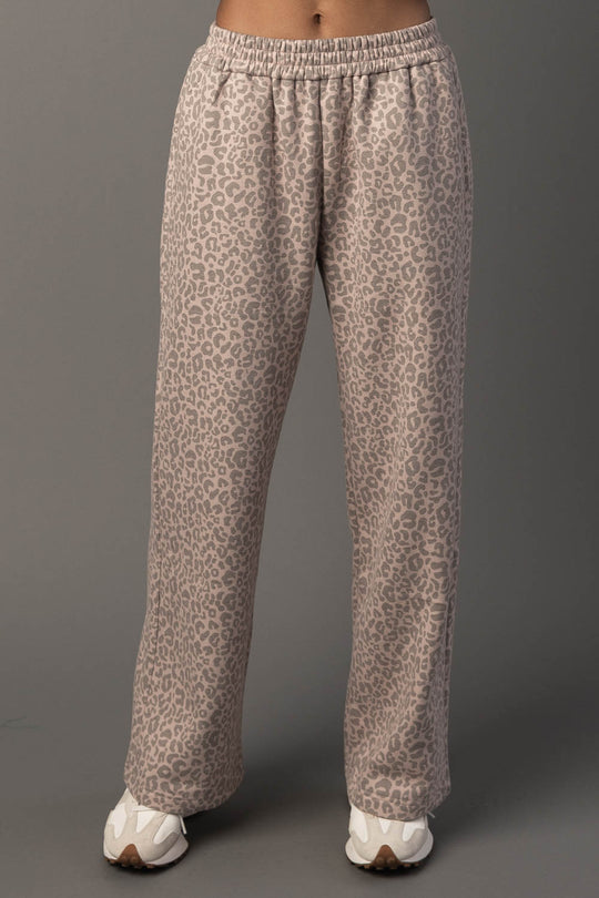 A person is wearing Blush & Light Brown Leopard Sweatpants by Panache Apparel Collection, paired with white sneakers, and standing against a plain gray background. The photo captures the sweatpants from waist to feet.