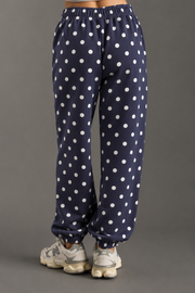 A person is shown from the back, wearing Panache Apparel Collection’s Navy & White Polka Dot Sweatpants featuring a cozy fleece texture, paired with white sneakers against a gray background. Only the lower half of the body is visible.