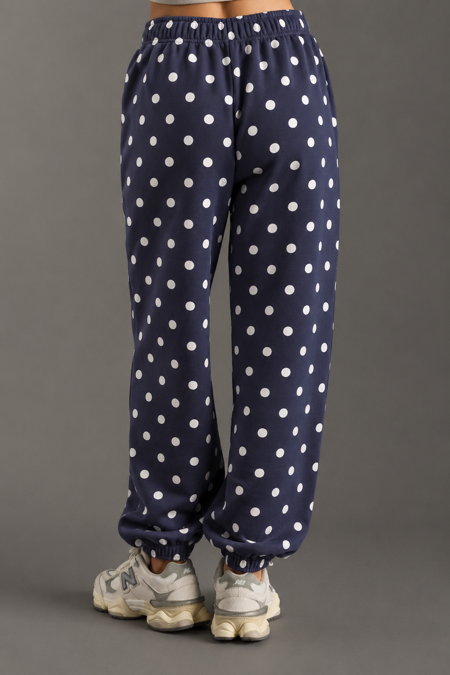 A person is shown from the back, wearing Panache Apparel Collection’s Navy & White Polka Dot Sweatpants featuring a cozy fleece texture, paired with white sneakers against a gray background. Only the lower half of the body is visible.