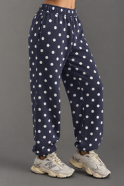 A person is shown from the waist down wearing Panache Apparel Collection’s Navy & White Polka Dot Sweatpants paired with beige New Balance sneakers, standing against a gray background.