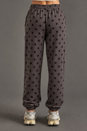 A person is seen from behind wearing Panache Apparel Collection’s Dark Gray & Black Polka Dot Sweatpants, paired with light gray sneakers and a coordinating dark gray and black sweatshirt. The minimalist ensemble stands out against a plain gray background.