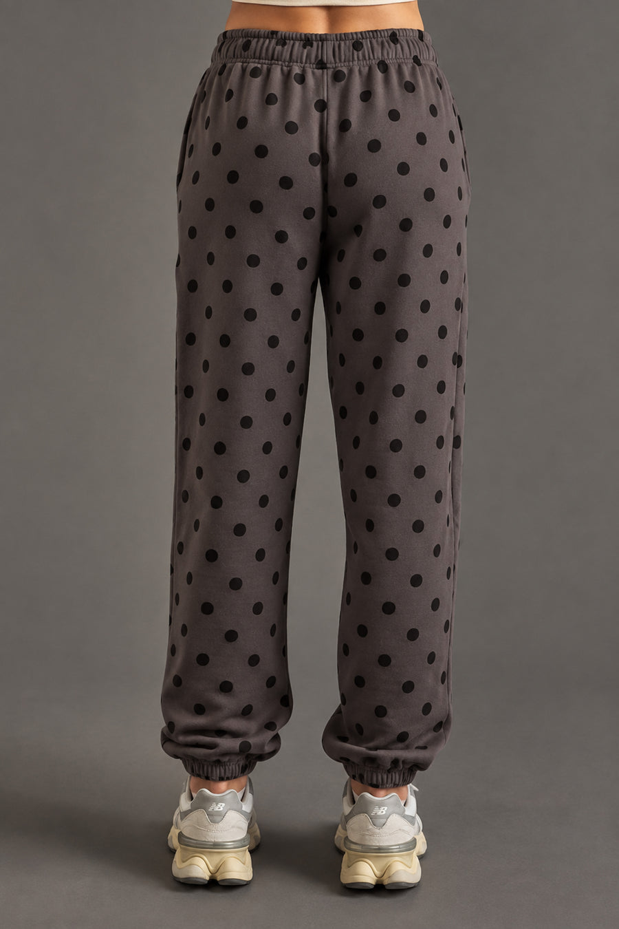 A person is seen from behind wearing Panache Apparel Collection’s Dark Gray & Black Polka Dot Sweatpants, paired with light gray sneakers and a coordinating dark gray and black sweatshirt. The minimalist ensemble stands out against a plain gray background.