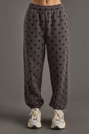 A person models the Panache Apparel Collection’s Dark Gray & Black Polka Dot Sweatpants with white sneakers, set against a plain gray background. The lower half of the outfit is shown, showcasing how these sweatpants pair effortlessly with an oversized fleece hoodie for a comfortable, casual vibe.