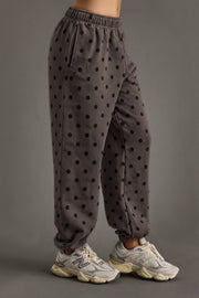 Wearing the Panache Apparel Collection’s Dark Gray & Black Polka Dot Sweatpants with white athletic shoes, this person stands against a plain gray background, effortlessly pairing the look with an oversized fleece hoodie for cozy coordination.