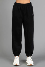 A person is wearing Black Panache Sweatpants from the Panache Apparel Collection, featuring an elastic waistband and cuffs, paired with white sneakers and standing against a plain gray background.