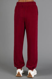 A person dressed in Maroon Panache Sweatpants by Panache Apparel Collection and white sneakers stands against a plain gray background. The photo is taken from behind, highlighting the back view of the sweatpants and shoes.