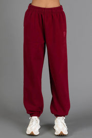 A person wearing the Maroon Panache Sweatpants from the Panache Apparel Collection, featuring an elastic waistband and cuffs, paired with white sneakers, stands against a plain gray background.