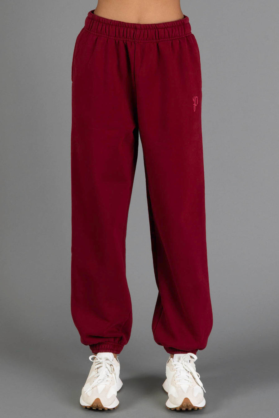A person wearing the Maroon Panache Sweatpants from the Panache Apparel Collection, featuring an elastic waistband and cuffs, paired with white sneakers, stands against a plain gray background.