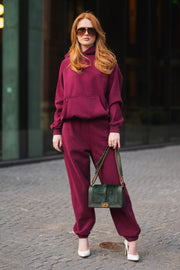 A woman wearing a matching maroon hooded sweatshirt and Maroon Panache Sweatpants, white high heels, and holding a dark green shoulder bag.