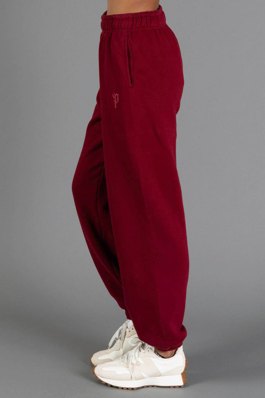 A person is wearing the Maroon Panache Sweatpants from the Panache Apparel Collection and white sneakers, standing sideways against a plain gray background.