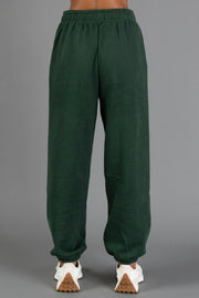 A person is wearing Panache Apparel Collection’s Dark Green Panache Sweatpants with white sneakers, standing against a plain gray background. The image displays the back view from the waist down.