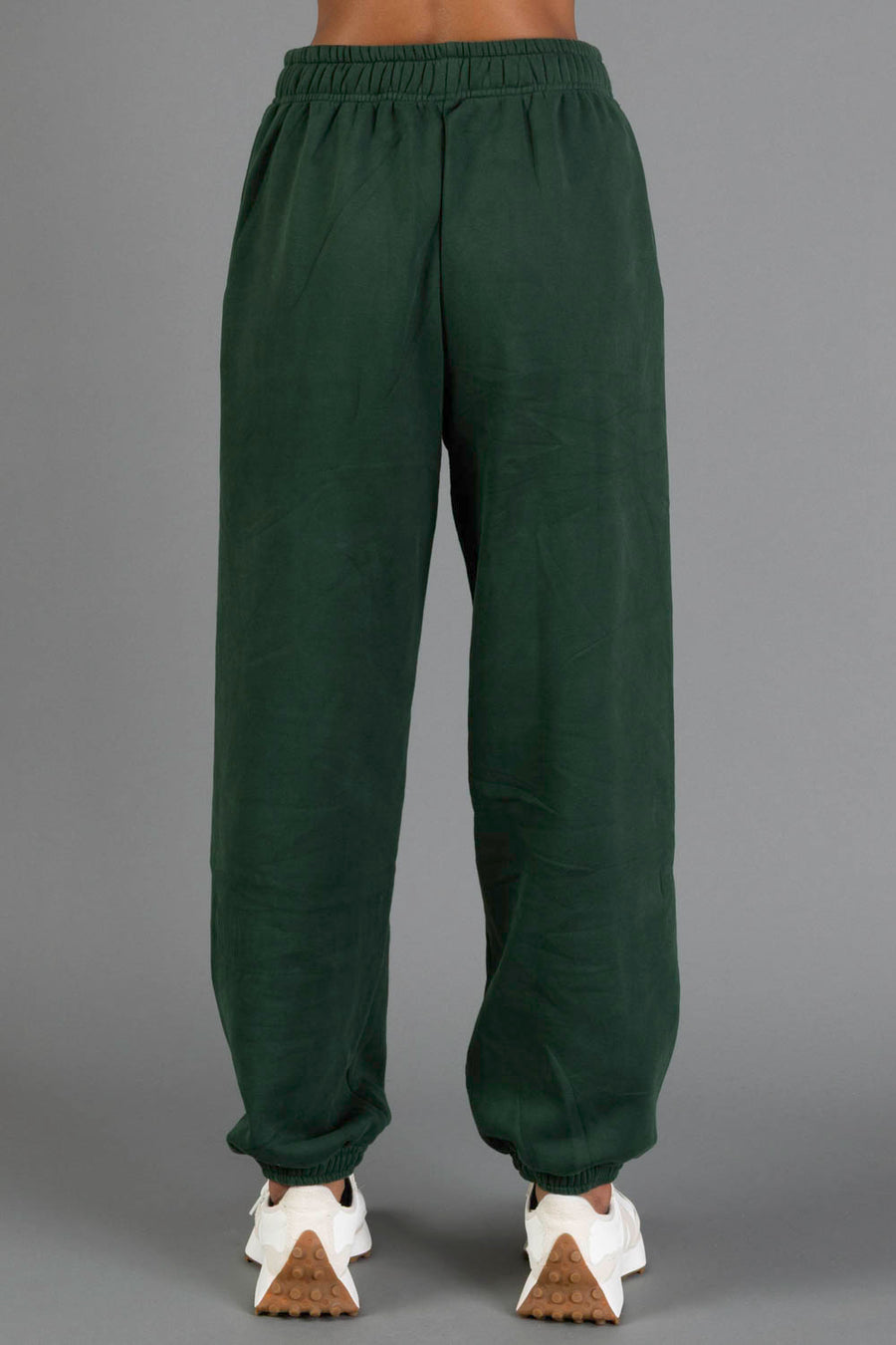 A person is wearing Panache Apparel Collection’s Dark Green Panache Sweatpants with white sneakers, standing against a plain gray background. The image displays the back view from the waist down.