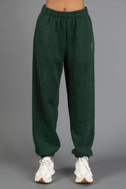 A person is wearing the Panache Apparel Collection’s Dark Green Panache Sweatpants, featuring an elastic waistband and cuffs, paired with white sneakers and standing against a plain gray background.