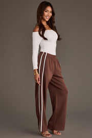 A person wears a white off-the-shoulder long-sleeve top and Brown Lounge Sweatpants from the Panache Apparel Collection featuring a double white side stripe.