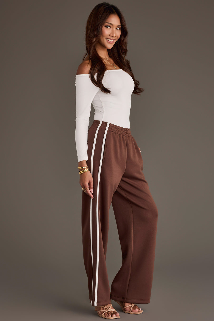 A person wears a white off-the-shoulder long-sleeve top and Brown Lounge Sweatpants from the Panache Apparel Collection featuring a double white side stripe.