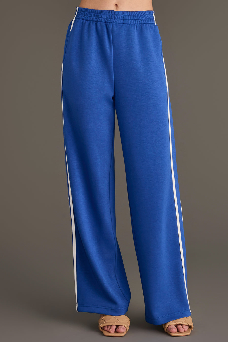 Blue Lounge Sweatpants featuring a wide-leg design with a white side stripe, an elastic waist, and tan slide sandals.