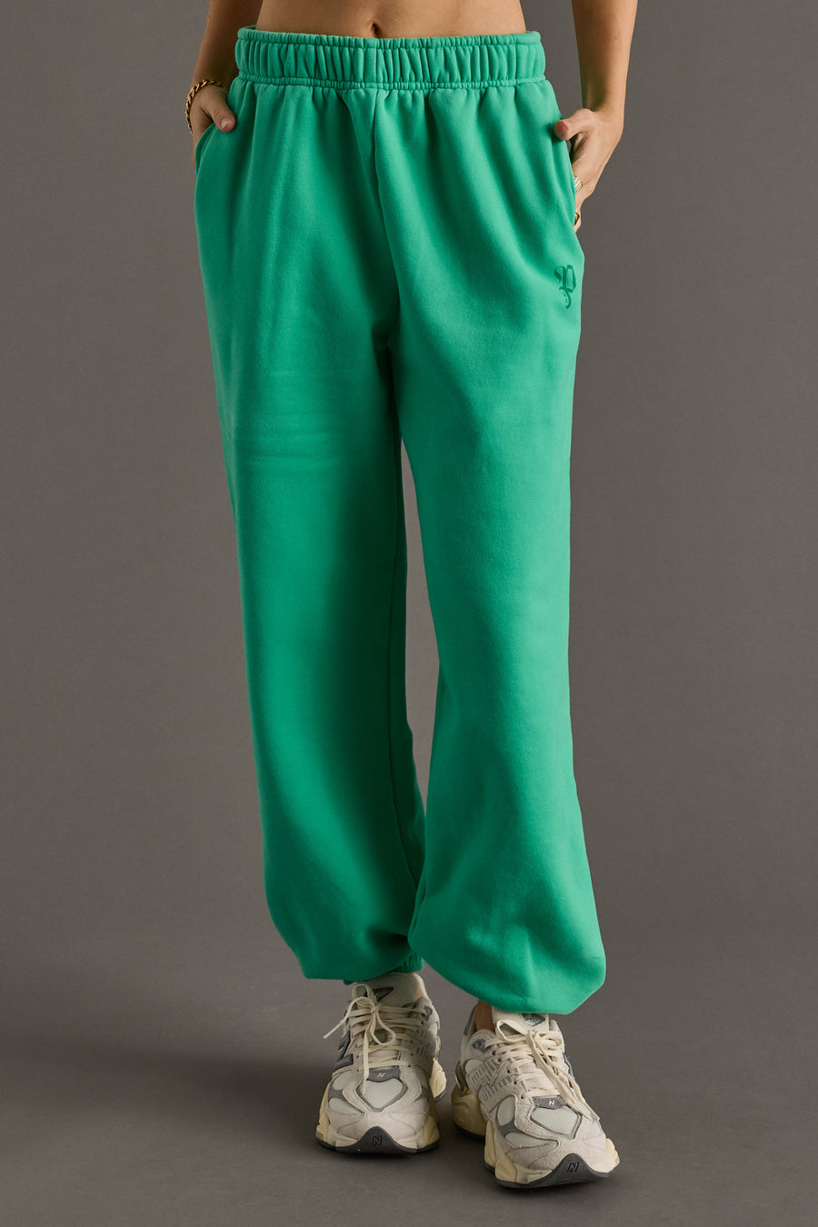 A person models the Green Panache Sweatpants from Panache Apparel Collection, featuring an elastic waistband, paired with white sneakers and hands in pockets. Only the lower body is visible against a plain gray background.
