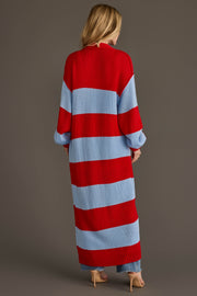 A woman with long blonde hair stands with her back to the camera, wearing the Panache Apparel Collection Red & Light Blue Striped Duster Cardigan, styled with light blue pants and nude heels.
