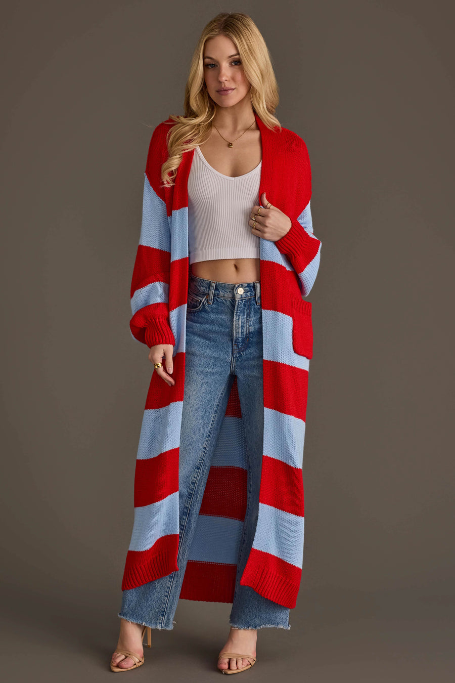 A woman stands against a plain brown background wearing the Panache Apparel Collection Red & Light Blue Striped Duster Cardigan, paired with a white crop top, blue jeans, and beige heels.