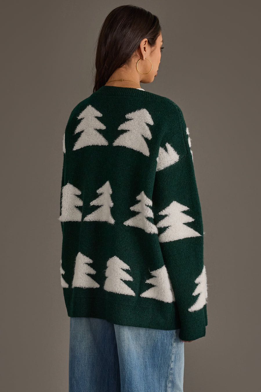 A person wears a Green Button Up Tree Cardigan from the Panache Apparel Collection, featuring a dark green, button-up design with a repeating white pattern of stylized evergreen trees.