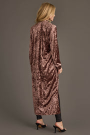 A woman with blonde hair models the Panache Apparel Collection Reddish-Brown Velvet Duster Cardigan, paired with black leggings and heels, standing with her back to the camera against a gray background.