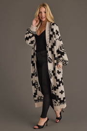 A woman models the Cream & Black Western Cardigan from Panache Apparel Collection, styled over a black top and pants with black heeled sandals, posing against a plain gray background.