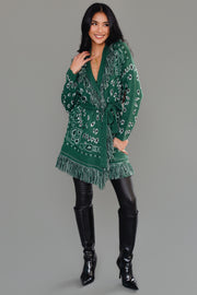 A woman with long dark hair is wearing the Panache Apparel Collection Green Bandana Fringe Cardigan with a belt, paired with black leather pants and gold jewelry, standing against a plain gray background.