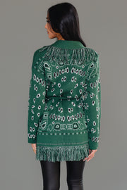 A woman models the Panache Apparel Collection Green Bandana Fringe Cardigan, paired with a black top, black leather pants, and black knee-high boots, standing against a gray background.