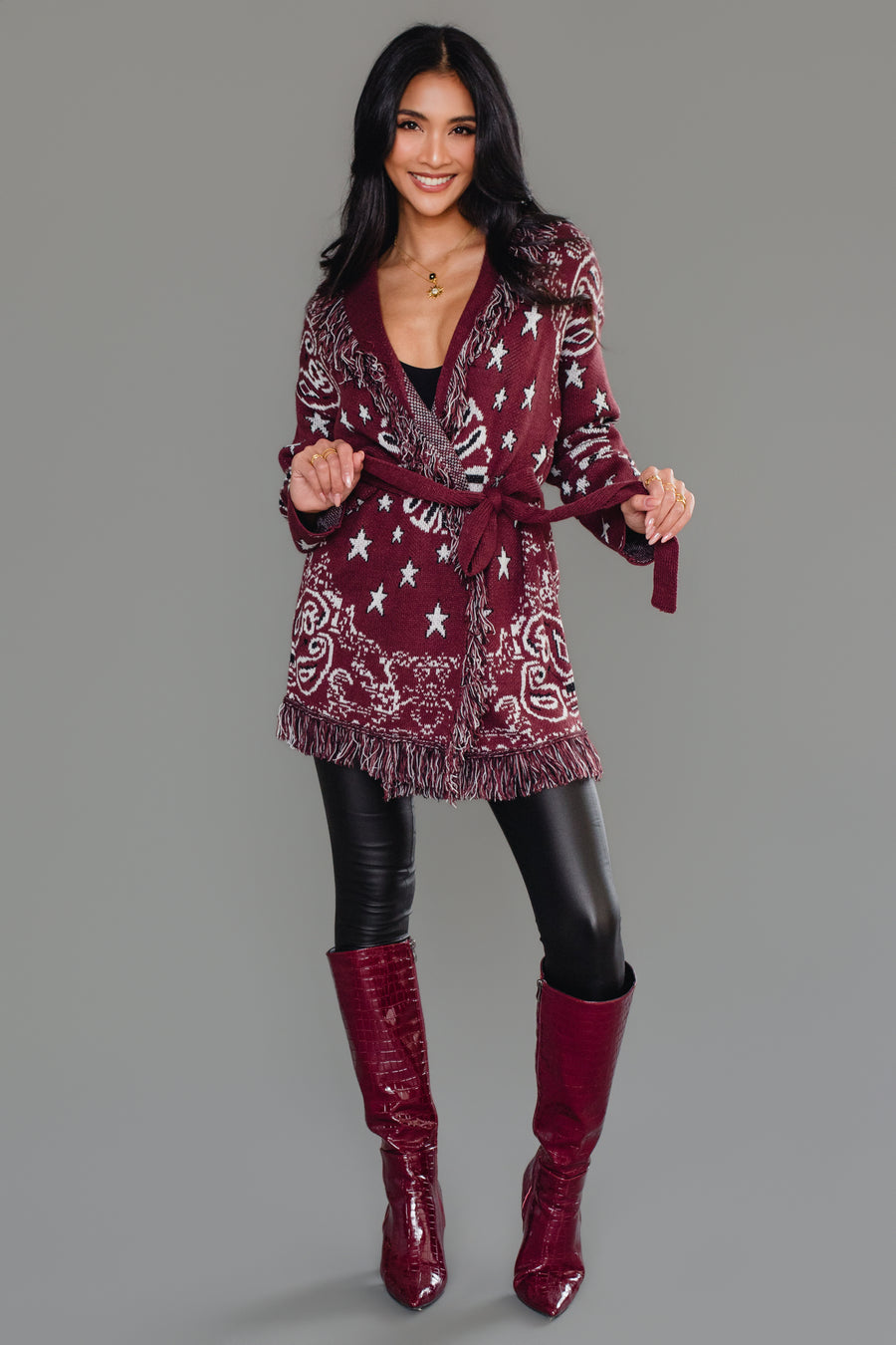 Full-length studio image of Panache Apparel’s burgundy bandana fringe cardigan with matching burgundy boots.