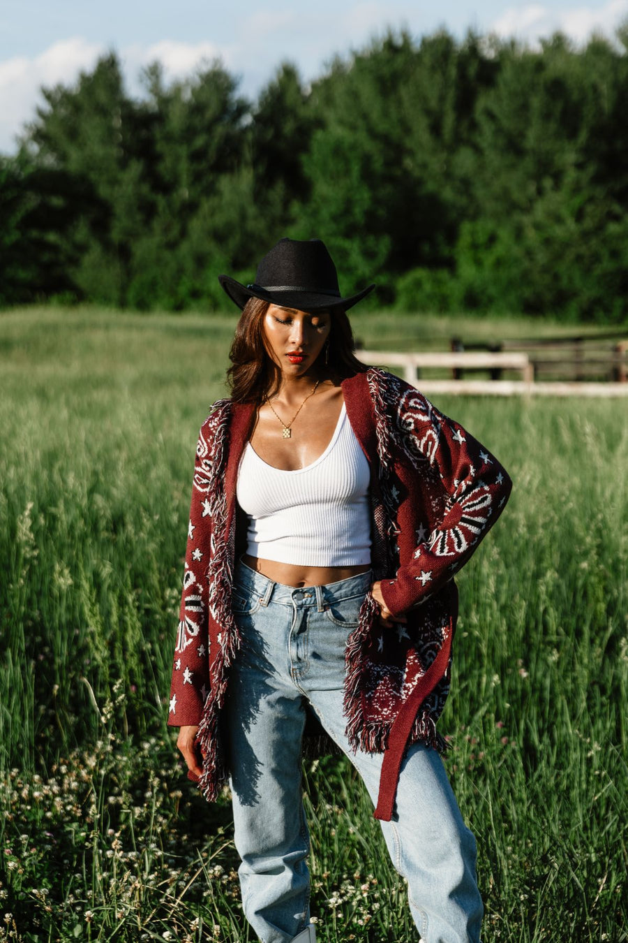 Woman wearing Panache Apparel’s burgundy bandana fringe cardigan outdoors, front view with black hat.