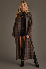 A woman is wearing the Brown, Cream & Blue Plaid Long Lightweight Jacket from Panache Apparel Collection over a black top and black shorts, paired with knee-high black boots, standing against a plain grey background.