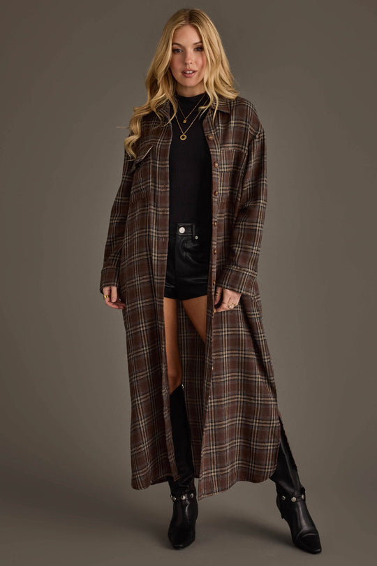 A woman is wearing the Brown, Cream & Blue Plaid Long Lightweight Jacket from Panache Apparel Collection over a black top and black shorts, paired with knee-high black boots, standing against a plain grey background.