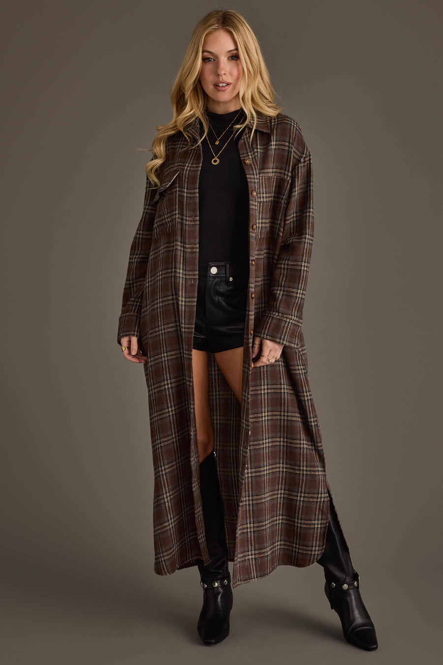 A woman is wearing the Brown, Cream & Blue Plaid Long Lightweight Jacket from Panache Apparel Collection over a black top and black shorts, paired with knee-high black boots, standing against a plain grey background.