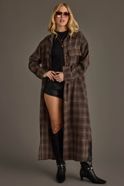 A woman stands confidently against a plain background, wearing sunglasses, a black turtleneck top, black leather shorts, black knee-high boots, and the Panache Apparel Collection’s Brown, Cream & Blue Plaid Long Lightweight Jacket.