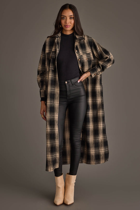 A woman is wearing the Panache Apparel Collection Black & Tan Plaid Long Lightweight Jacket over a black top and black skinny pants, paired with tan ankle boots, against a plain gray background.