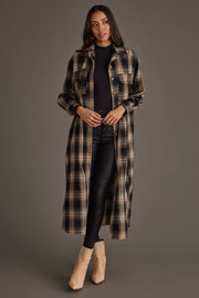 A woman with long dark hair and a neutral expression stands against a gray background, wearing the Panache Apparel Collection Black & Tan Plaid Long Lightweight Jacket over a black top and black pants, paired with beige ankle boots.