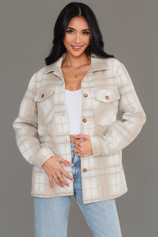 A woman stands against a plain gray background, smiling as she holds the front of her Panache Apparel Collection Tan, Cream & Gray Plaid Jacket, styled over a white top and blue jeans.