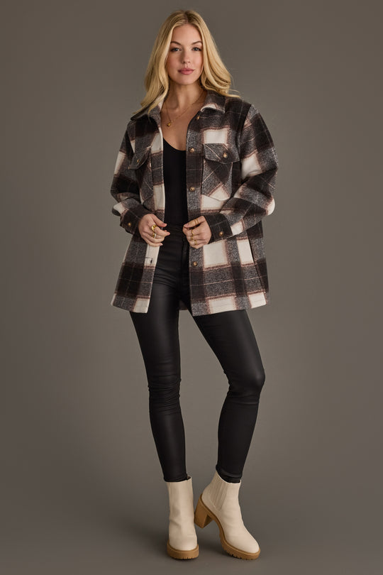 A woman stands against a plain background wearing the Panache Apparel Collection Black, Brown & White Plaid Jacket over a black top and black pants, paired with light-colored ankle boots.