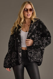 Blonde model wearing Panache Apparel’s black and white paisley fleece coatigan with sunglasses and black leather pants.