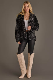 Full-length model wearing Panache Apparel’s black and white paisley fleece coatigan with black pants and cream western boots.