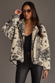 A woman wearing sunglasses, a black top, black leather pants, and the Panache Apparel Collection White & Black Paisley Fleece Coatigan poses against a plain gray background.