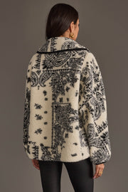 A woman with long dark hair models the Panache Apparel Collection White & Black Paisley Fleece Coatigan, facing away to highlight the intricate paisley pattern on the back. She accessorizes with gold hoop earrings and rings.