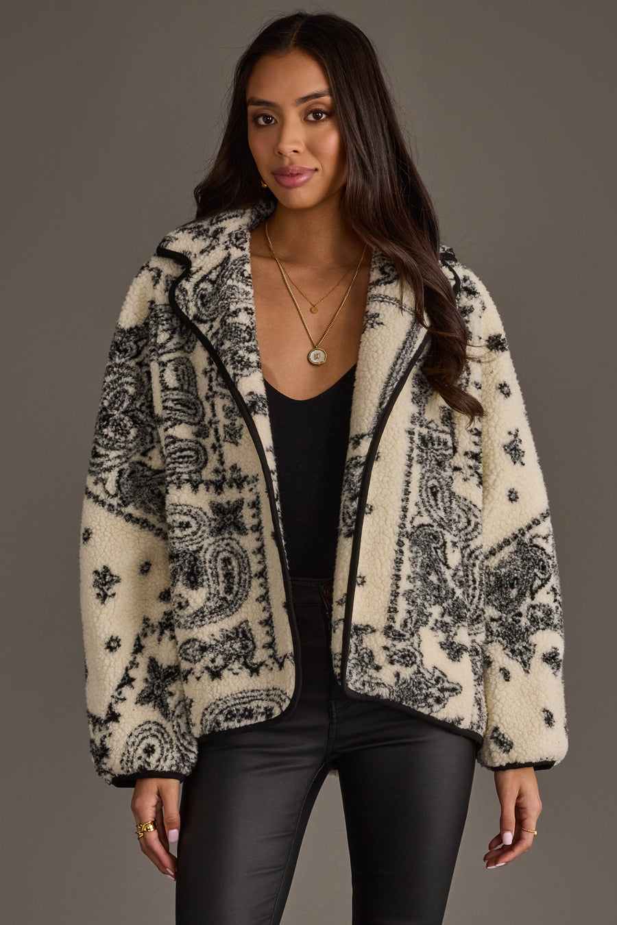 A woman wearing a black top, black leather pants, and the Panache Apparel Collection White & Black Paisley Fleece Coatigan stands against a plain background, looking at the camera with a slight smile.
