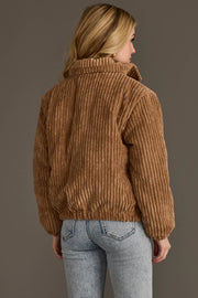 A person with long blonde hair is shown from the back against a gray background, wearing the Panache Apparel Collection’s Tan Corduroy Puffer Jacket and light blue jeans.