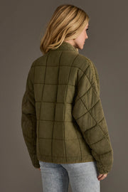 A person with blonde hair wears the Panache Apparel Collection Olive Soft Quilted Jacket and light blue jeans, standing against a plain gray background and facing away from the camera.