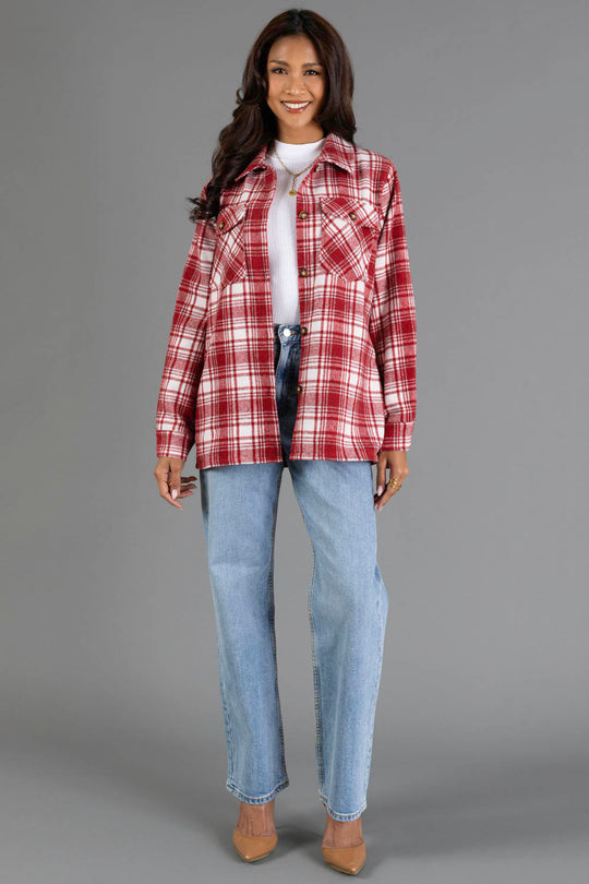 A woman stands smiling against a plain gray background, wearing the Panache Apparel Collection’s Red & White Plaid Jacket over a white top, paired with light blue jeans and beige heels.