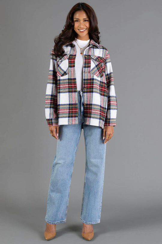 A woman stands and smiles, wearing the Panache Apparel Collection Ivory & Multicolored Plaid Jacket over a white top, paired with light blue jeans and beige heels. She has long, wavy dark hair and is posed against a plain gray background.
