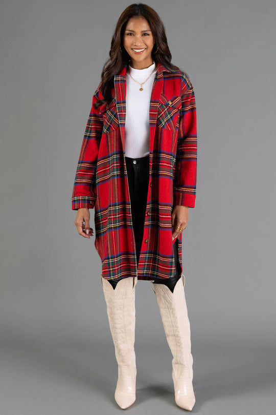 A woman wearing the Panache Apparel Collection Red, Green, Blue & Yellow Plaid Long Shacket over a white top, black skirt, and cream knee-high boots stands smiling against a plain gray background.